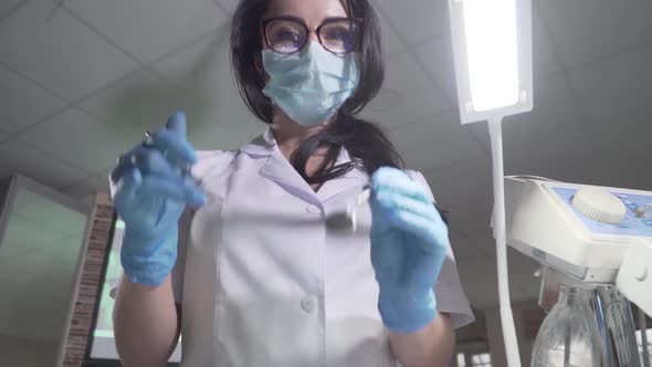 Bottom View of Young Professional Female Stomatologist Approaching To Camera with Dental Instruments alt
