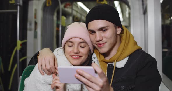 Millennial Couple Watching Funny Video on Smartphone and Laughing While Sitting Together in Bus alt