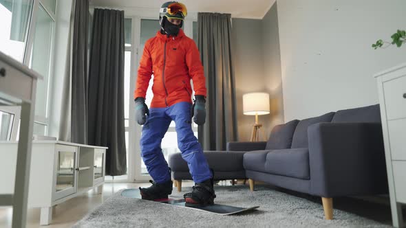 Fun Video. Man Dressed As a Snowboarder Rides a Snowboard on a Carpet in a Cozy Room. Waiting for a alt
