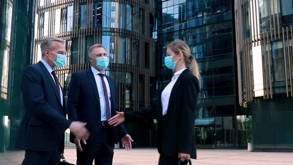 Two Businessmen in Medical Mask Meet a Businesswoman Also Wearing a Mask and Shake Hands with Her