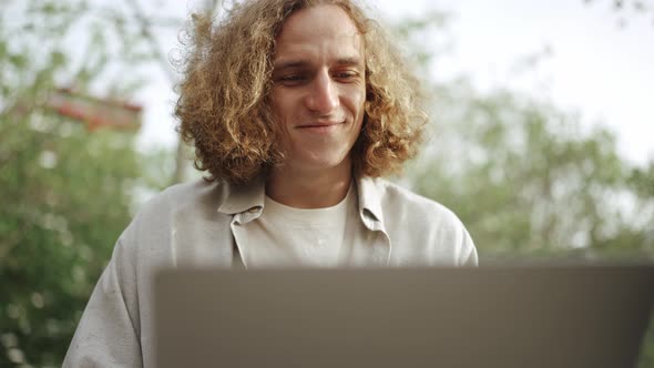 Smiling curly-haired man working on laptop alt