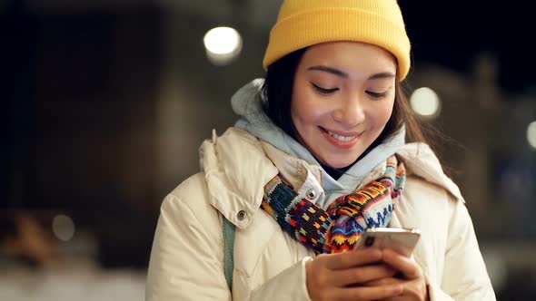 Asian woman at the evening winter street holding mobile phone