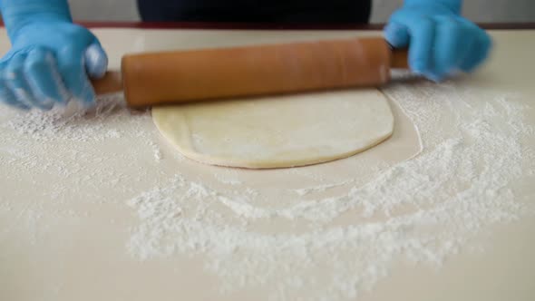 Rolls Out the Dough on the Kitchen Table. Female Hands Rolling Dough with a Rolling Pin, Close Up alt
