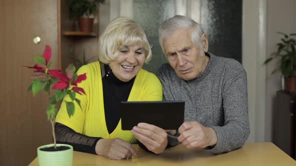 Pretty Mature Senior Couple Grandparents Enjoy Online Shopping on Tablet at Home alt