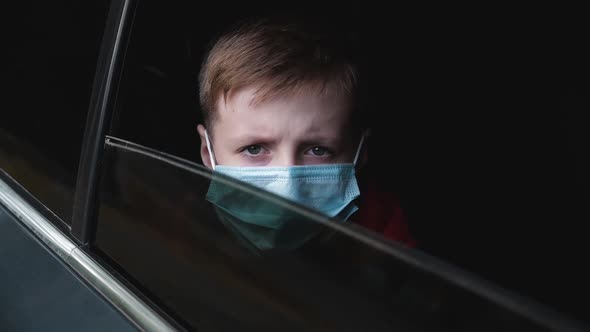 Young Boy in a Medical Mask Looks Through the Car Window and Lifts the Glass.