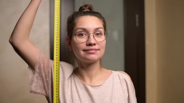 A young woman shows joy at her growth by holding a measuring tape next to her alt
