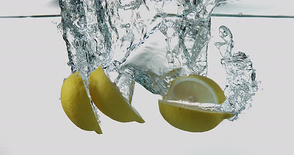 Yellow Lemons, citrus limonum, Fruits falling into Water against White Background, Slow Motion 4K alt