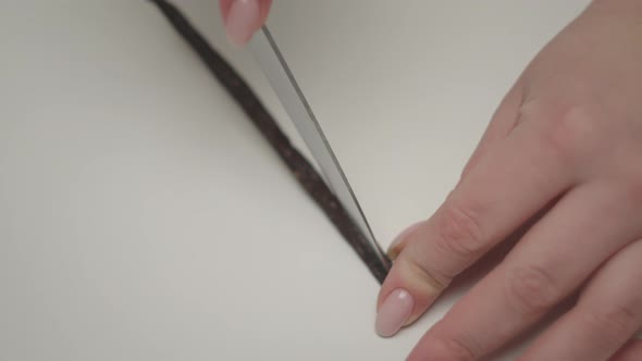 Female hands cutting vanilla pod with knife on white table in slow motion. alt