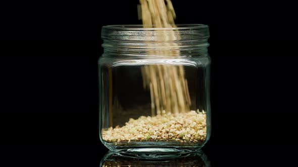 Closeup of Falling Down Green Buckwheat Into Glass Jar on Black Background alt