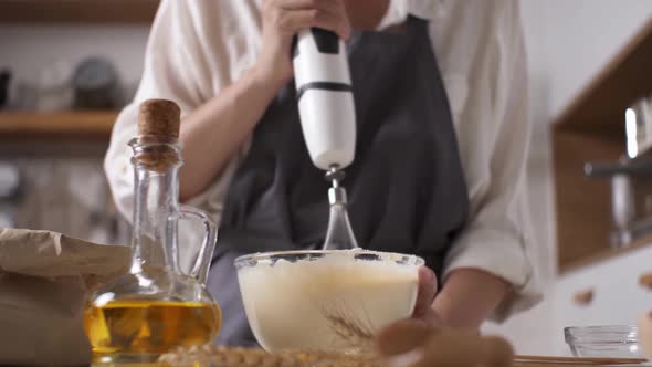 Whipping Dough For Pancakes With Mixer. Immersion Blender With Whisk Girl Dough In Glass Bowl alt