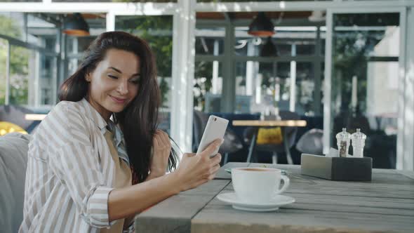 Cheerful Young Lady Taking Selfie with Smartphone Camera Posing in Outdoor Cafe alt