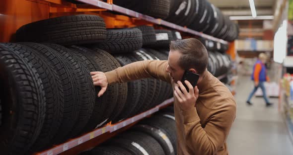 Man Chooses Winter Car Tires in Auto Shop Consulting By Smartphone alt
