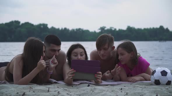 Beautiful Young People Lie with a Tablet on the Beach By the River alt