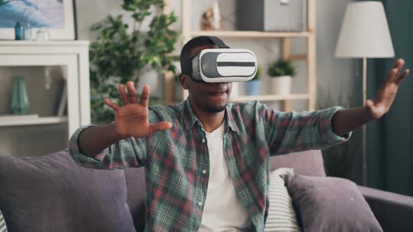 African American Young Man Is Playing Game in Augmented Reality Glasses Having Fun Alone at Home alt