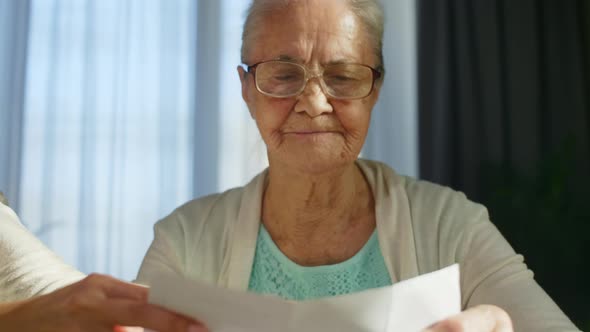 Elderly Woman Putting on Glasses and Reading Document