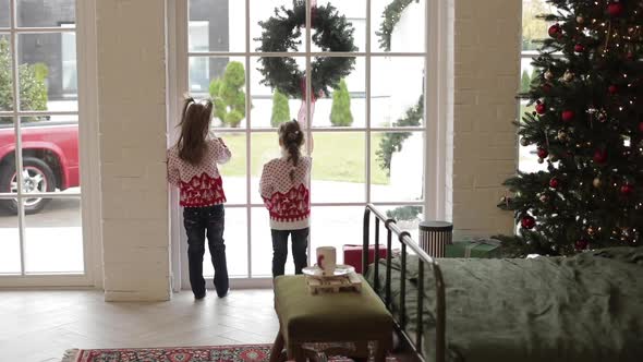 Beautiful Little Sisters Waiting for Parents at Home and Looking Out the Window