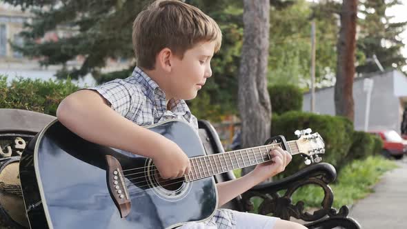 Portrait of a Cute Pretty European Teenager Sitting on a Bench Outdoors Playing an Acoustic Guitar