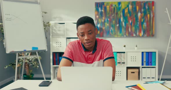 A Young Boy of African American Beauty Sits at Desk in an Office Room with a Laptop Smiles Broadly alt
