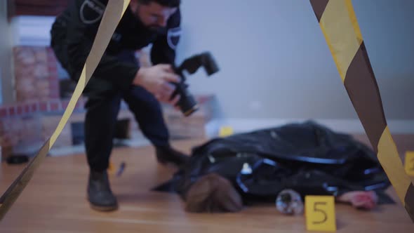 Blurred Caucasian Detective Opening Body of Murder Victim and Taking Photos. Focused on Police Tape alt