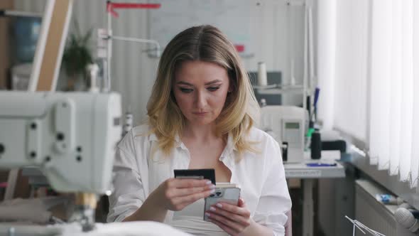 Young Beautiful Light Hair Seamstress Uses Smartphone in the Workplace