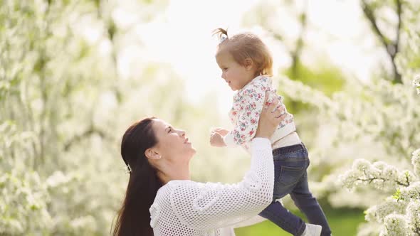 Mom Throws Up Her Daughter in the Park By a Flowering Tree alt