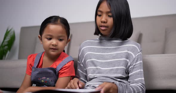 Handheld shot of The older sister teach the younger sister to read book alt