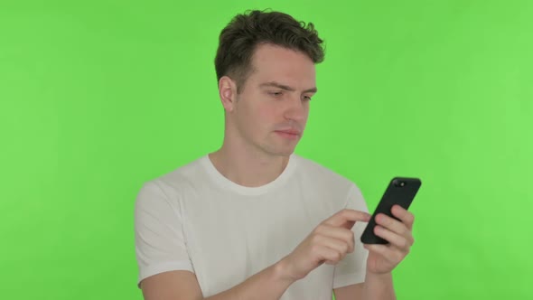 Young Man Browsing Smartphone on Green Background alt