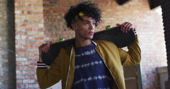 Portrait of african american man carrying skateboard standing in empty parking garage alt