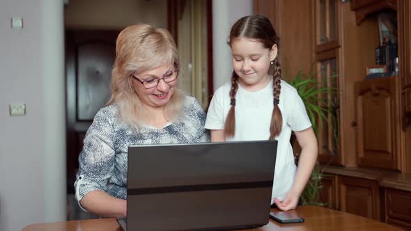 Little young school age girl teaching grandmother using laptop notebook tech at home. Slow motion alt