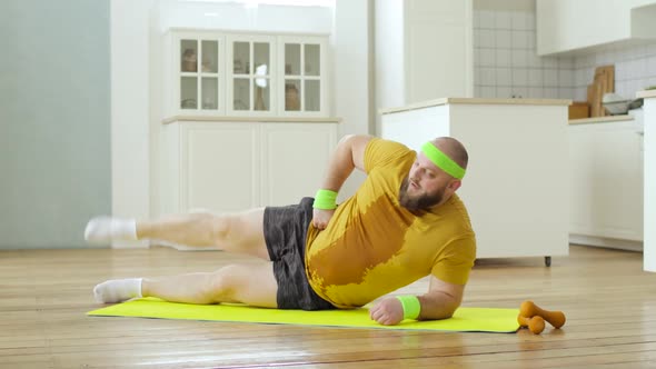 Sweat Fat Man in Yellow Wet Sportswear Doing Legs Lifting Exercise Lying on Mat