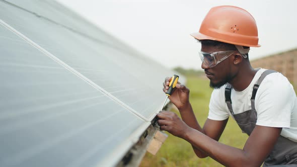 Technician in Helmet and Overalls Fixing Solar Panels with Screwdriver Outdoors alt