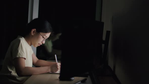 A young woman writes an article on a tablet at night in a home office.