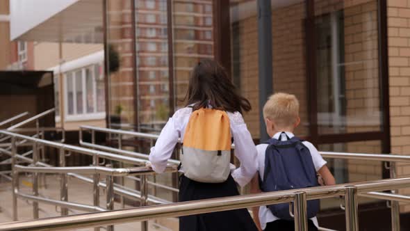 Small Children with Backpacks Run Through the School Yard to the Entrance alt