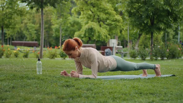 Woman standing in plank in the park on yoga mat, endurance effort alt