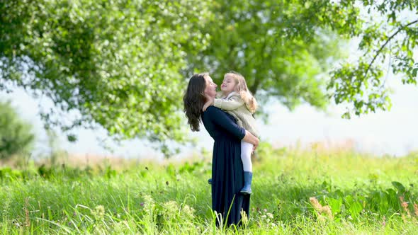 Mother gently hugs and kisses her beloved daughter outdoors.