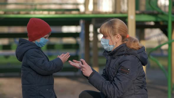 Hand Sanitizer in a Public Place. A Mother in a Medical Mask Splashes the Product on the Child's
