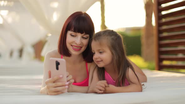 Relaxed Young Woman and Her Daughter Watching Movie or Having Video Chat on Smartphone alt