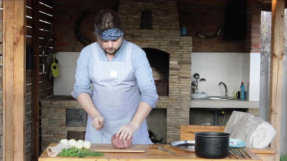 Cheerful Man Cuts Meat for Barbecue on the Street in the Gazebo alt