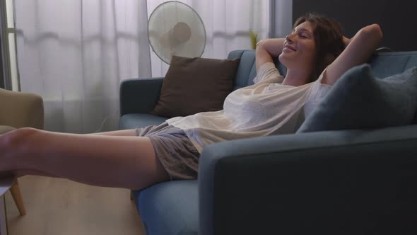 Happy woman lying on the sofa and cooling herself at home