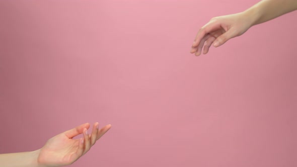 Close up of two hands touch the fingertips on light pink background. alt
