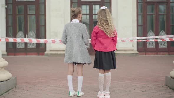 Wide Shot of Two Girls Standing in Front of Closed School During Coronavirus Lockdown. Sad alt