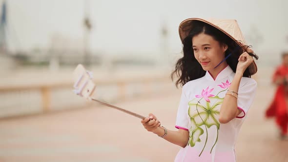 The Girl in the Vietnamese National Traditional Costume Photographs Herself Using the Phone alt