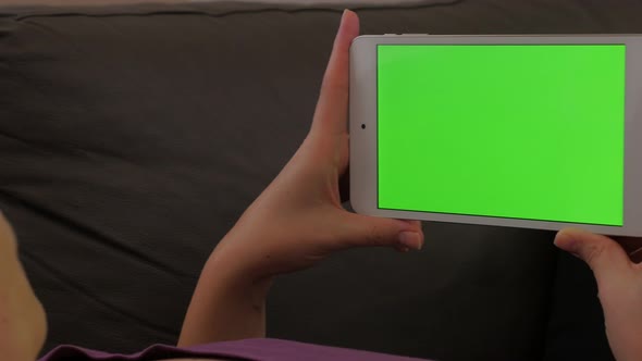 Young woman relaxing in bed while looking to greenscreen display on silver tablet 4K 3840X2160 UHD v