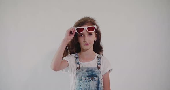 Young caucasian girl lifting her glasses with red lenses and looking at the camera.