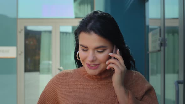 Young Hispanic Woman Walking Street Background Office Building Talking on Mobile Telephone Smiling alt