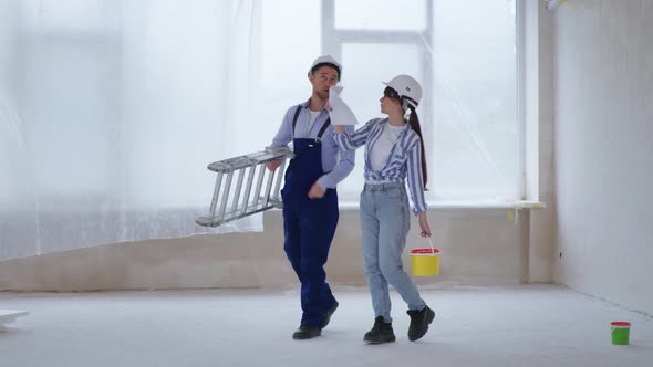 Woman in Protective Helmets with Stepladder and Bucket of Paint in Their Hands Discussing Color alt