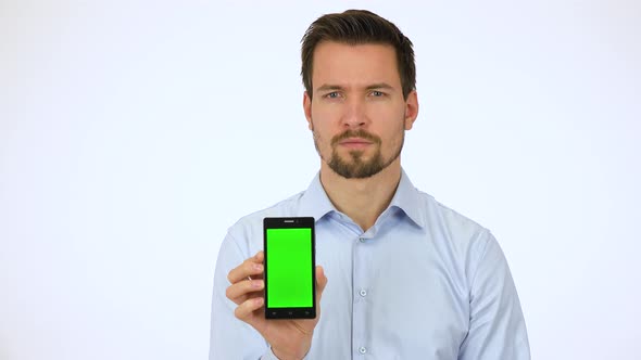 A Young Man Shows a Smartphone with Green Screen To the Camera and Slowly Smiles - White Screen alt