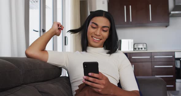 Gender fluid male smiling while using smartphone sitting on the couch at home alt