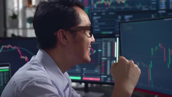 Asian Male Stock Market Broker Celebrating With Analyzing Graphs On Multiple Computer Screens alt