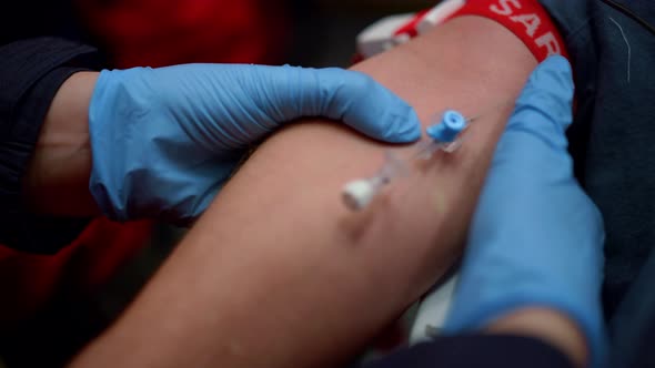 Emergency Doctor in Gloves Inserting Needle of Intravenous Catheter Into Man Arm alt